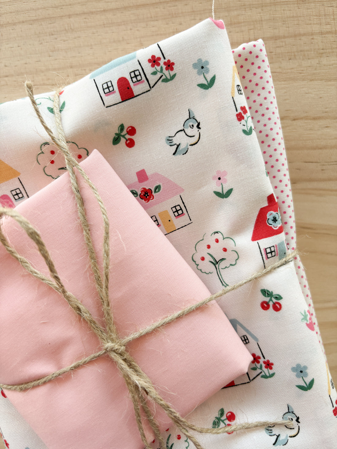 Bundle of fabric with cute cottages birds and trees with white and pink tied with twine.