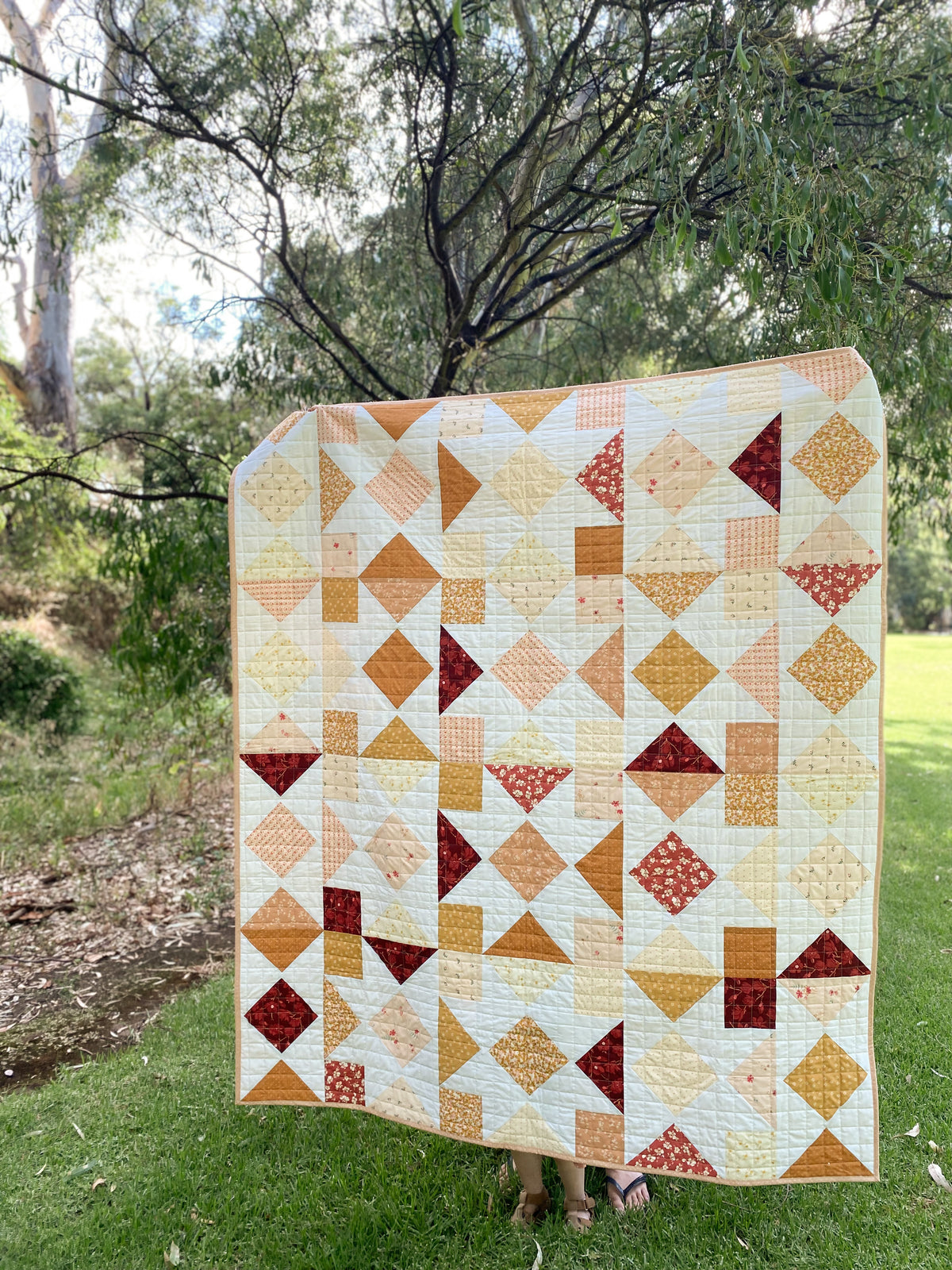 Modern Quilt fresh modern pattern with Burgundy Mustard white colours held up in picturesque park setting