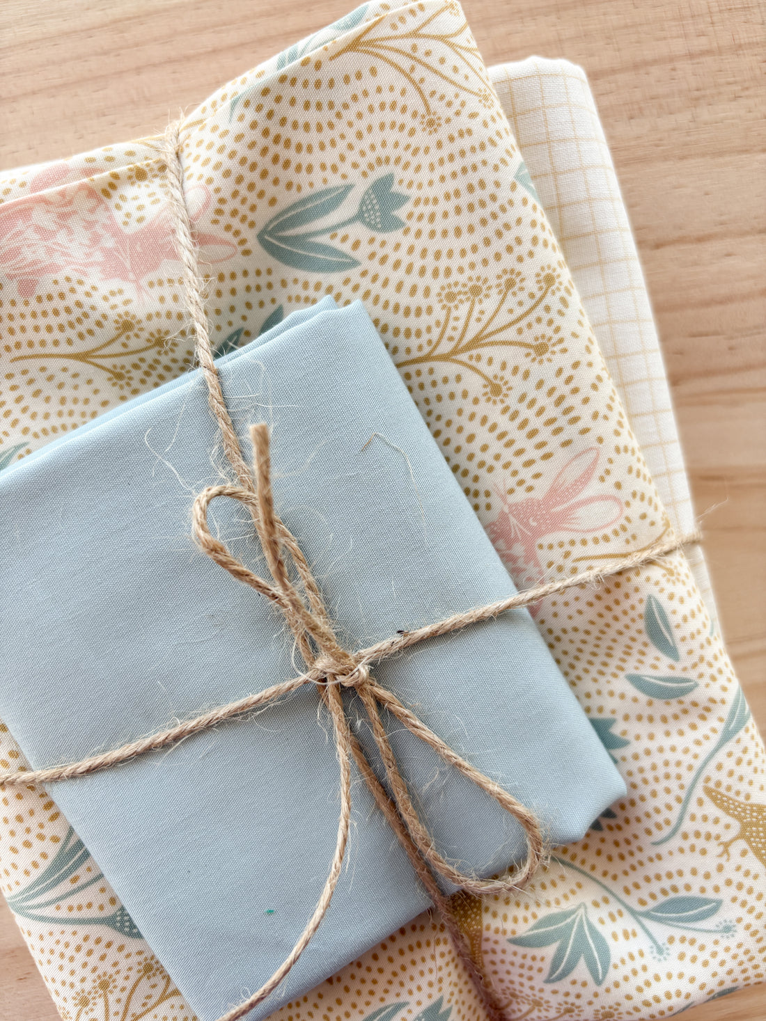 Fabric bundle with bunnies in fields with blue, cream, and mustard browns tied with twine